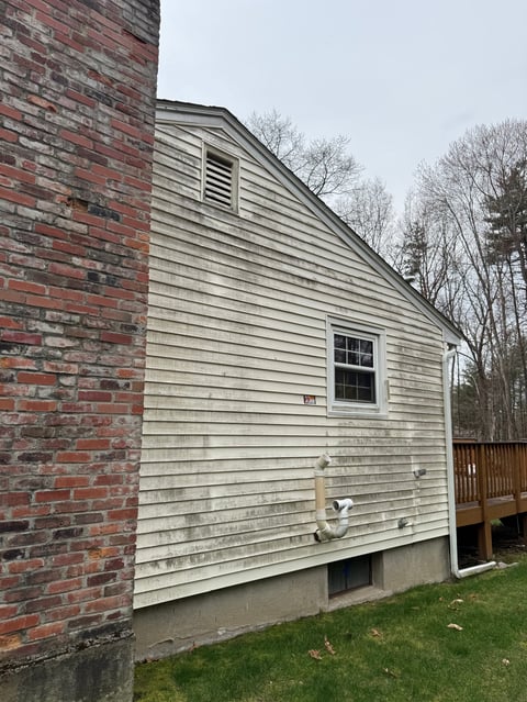 Side view of a single-story house with light green siding, red brick chimney, and wooden deck against bare trees